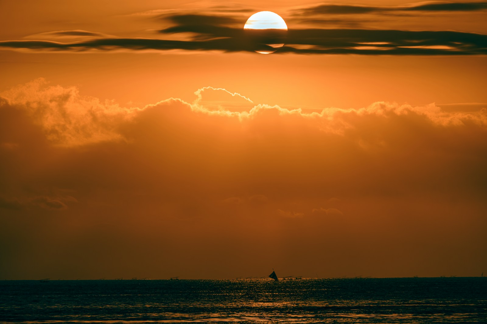 the sun is setting over the ocean with a sailboat in the distance